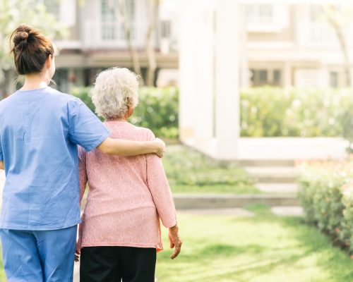 Back view of nurse caregiver support walking with elderly woman outdoor