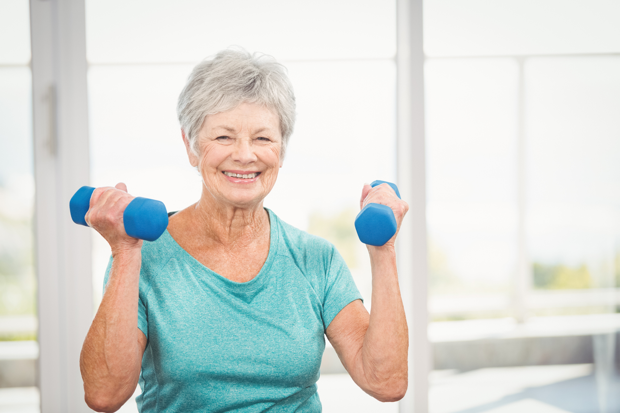 Portrait of happy senior woman holding dumbbell at home