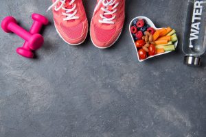 Fitness concept, pink sneakers, dumbbells, bottle of water and heart shaped plate with vegetables and berries on a beton background, top view, healthy lifestyle