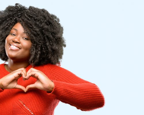 Beautiful african woman happy showing love with hands in heart shape expressing healthy and marriage symbol, blue background