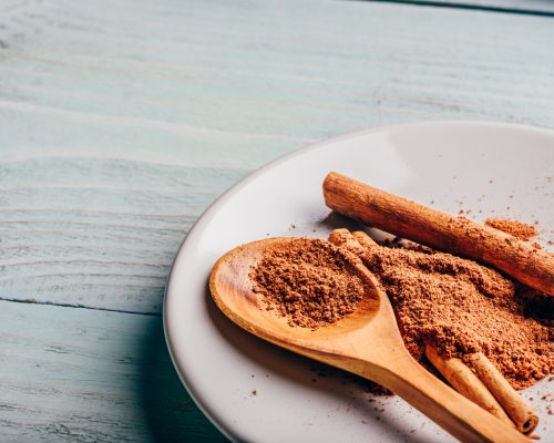 Cinnamon sticks and ground spice on white plate over light wooden background.