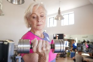 Senior Woman Exercising With Weights In Gym
