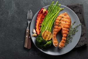 Tasty and healthy salmon steak with asparagus, broccoli and red pepper on a gray plate. Diet food on a dark background with copy space. Top view. Flat lay.