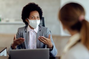 African American bank manager with protective face mask communicating with her client during a meeting in the office.