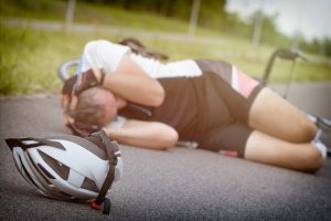 Cyclist lying on the road and holding his head, helmet in foreground