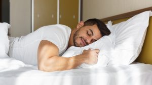 Young eastern man peacefully sleeping in his bed, panorama with copy space