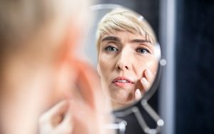 Skin Aging. Pretty Mature Woman Looking In Mirror Touching Face Standing In Bathroom At Home. Selective Focus