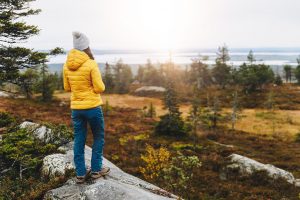 Woman traveler in yellow jacket from back hike in autumn forest in Finland Lapland. Hiking travel and adventure.