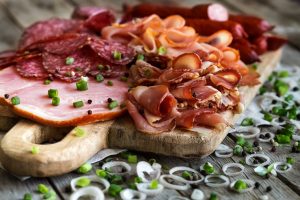 Mix of meat appetizers - salami, ham, smoked turkey, sausages and prosciutto - on rustic wooden background