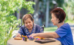 Elderly woman with caregiver in the needle crafts occupational therapy for Alzheimer’s or dementia