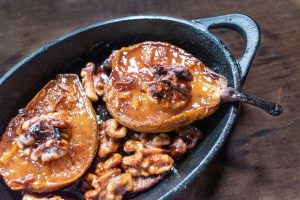 small cast iron dish of roasted pear halves with walnuts and sugar glaze top view