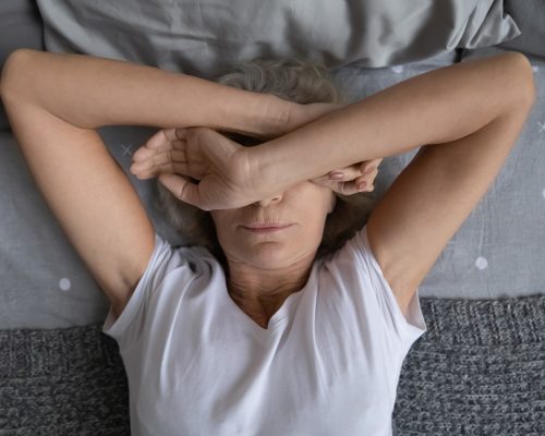 Top view aged woman lying on bed woke up at night due noisy neighbors. Mature female cover face with hands suffers from insomnia sleep disorder, has restless obsessive thoughts keep her awake concept