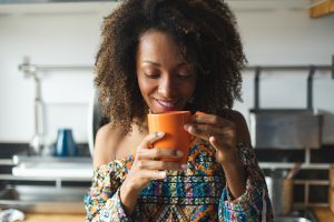 Casual young black woman taking a relaxing cup of coffeee in the kitchen at home. Afro hairstyle model.