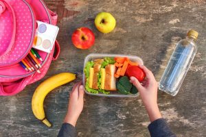 Sandwiches, fruits and vegetables in food box, backpack on old wooden background. Concept of child eating at school. Top view. Flat lay.