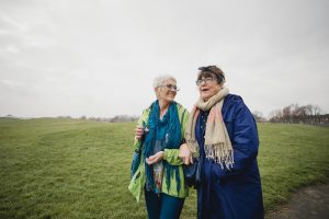 Two senior female friends walking in the park together, laughing and smiling.