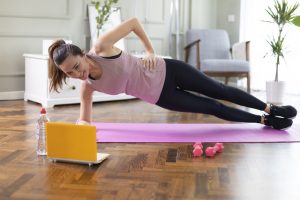 Young woman exercising at home in a living room. Video lesson. She is repeating exercises while watching online workout session.
