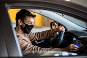 A young man drives a car with a mask on his face and adjusts the music in the car, life during a pandemic caused by a virus