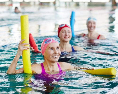 Smiling mature female in swimwear and two more active women listening to trainer advice during gymnastics in water