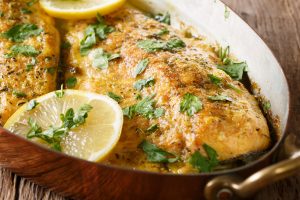 Delicious food: trout fish with garlic lemon butter sauce, parsley close-up in a copper frying pan on the table. horizontal