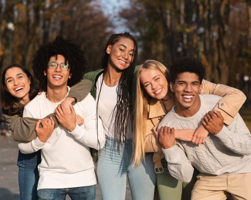 Positive group of multiracial young friends having fun at public park, hugging and smiling