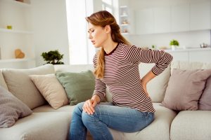 Close up side profile photo beautiful she her lady arms hands hold back spine suffering terrible pain wear jeans denim striped pullover clothes bright comfort flat house living room indoors.