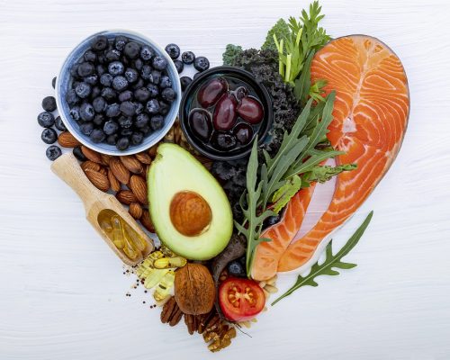 Heart shape of ketogenic low carbs diet concept. Ingredients for healthy foods selection on white wooden background. Balanced healthy ingredients of unsaturated fats for the heart and blood vessels.