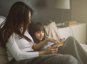 mother and daughter reading book at home in the bedroom