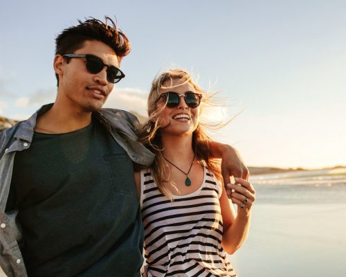 Portrait of handsome young man with his beautiful girlfriend on beach. Young couple enjoying a summer day on seashore.