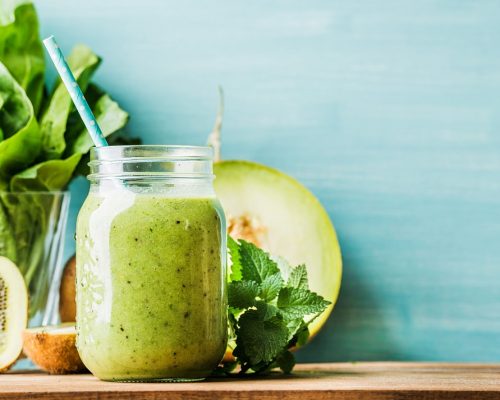 Freshly blended green fruit smoothie in glass jar with straw. Turquoise blue background, copy space