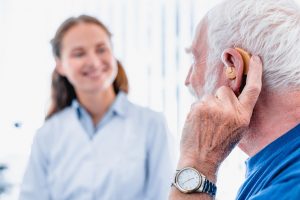 Focused picture of an elderly male patient with hearing aid side view with blurred woman doctor in the background