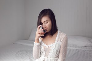 Asian woman in white nightgown drinking water on the bed at bedroom
