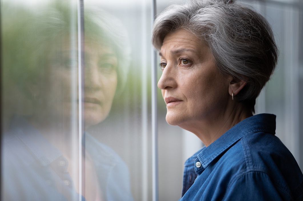 Close up thoughtful upset mature woman looking out window at home alone, sad senior grey haired female lost in thoughts, thinking about problem, nostalgia and melancholy, feeling lonely
