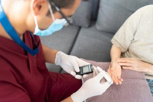 Young male nurse checks elderly patient’s blood sugar at home