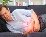 Man feeling stomach bloating and stomachache lying on the sofa