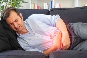 Man feeling stomach bloating and stomachache lying on the sofa