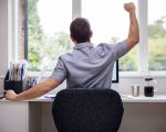 Rear View Of Man Working From Home On Computer In Home Office Stretching At Desk