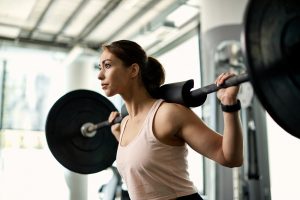 Young athletic woman exercising with barbell during weight training in a gym.