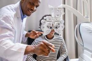 African young woman girl doing eye test checking examination with male man optometrist using phoropter in clinic or optical shop. Eyecare concept.
