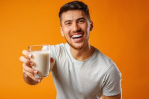 Happy smiling mixed-race man holding milk against yellow background close up