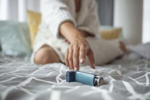 Girl suffering asthma attack reaching inhaler sitting on a bed in the bedroom at home. Woman Hand Reaching Inhaler Because She Suffering From Asthma Attack