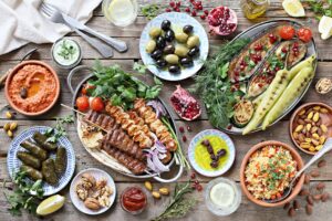 Middle eastern, arabic or mediterranean dinner table with grilled lamb kebab, chicken skewers with roasted vegetables and appetizers variety serving on rustic outdoor table. Overhead view.