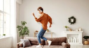 Positive young lady in wireless headphones and casual clothes listening to music with pleasure and dancing of sofa in light mo