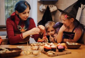 Mother and her daughters having fun at home. Happy Family preparing for Halloween. Mum and kids taste, decorated festive fare at kitchen.