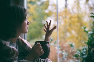 Fall melancholy mood concept. Wistful woman sitting near window and looking at autumn landscape outside in rainy day. Copy space.