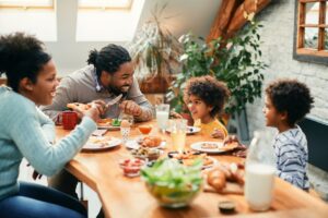 Happy black parents and their kids talking while having breakfast together in dining room.