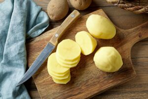 fresh raw peeled sliced potatoes on rustic wooden kitchen cutting board, top view
