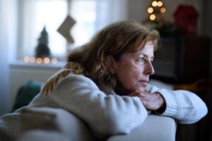Portrait of lonely senior woman sitting on sofa indoors at Christmas, solitude concept.