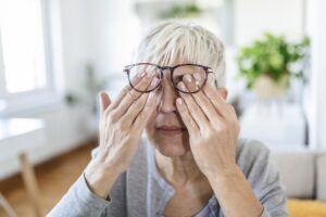 Mature woman holds glasses with diopter lenses,rubs her eyes and looks through them, the problem of myopia, vision correction