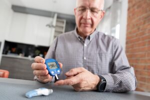 Senior man with glucometer checking blood sugar level at home. Diabetes, health care concept