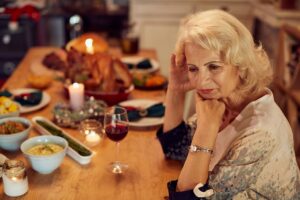 Sad mature woman feeling lonely and missing her family at dining table on Thanksgiving.